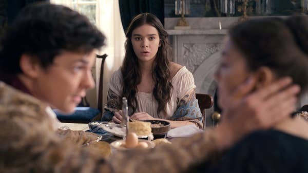 A woman with long dark hair sits at a breakfast table, looking across the table at another woman and a man. The woman looks concerned, looking at the other woman who has the man's hand on her face.