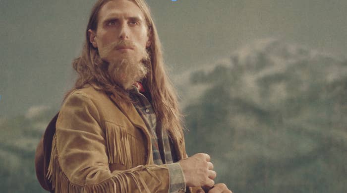 A man dressed as a cowboy with a long beard stares into the distance