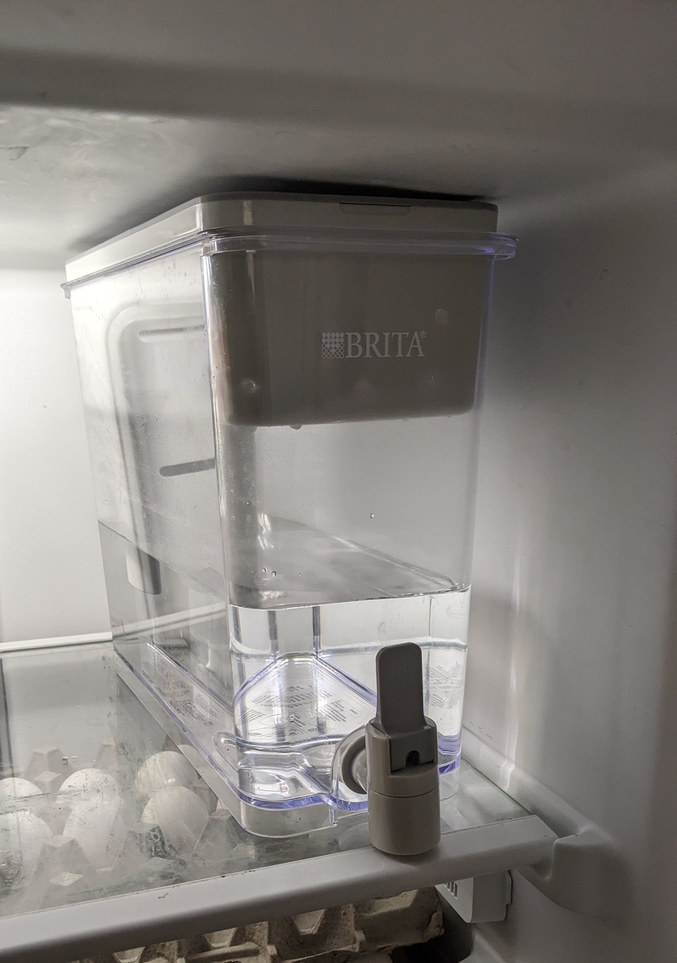 A large water dispenser on the top shelf of a fridge