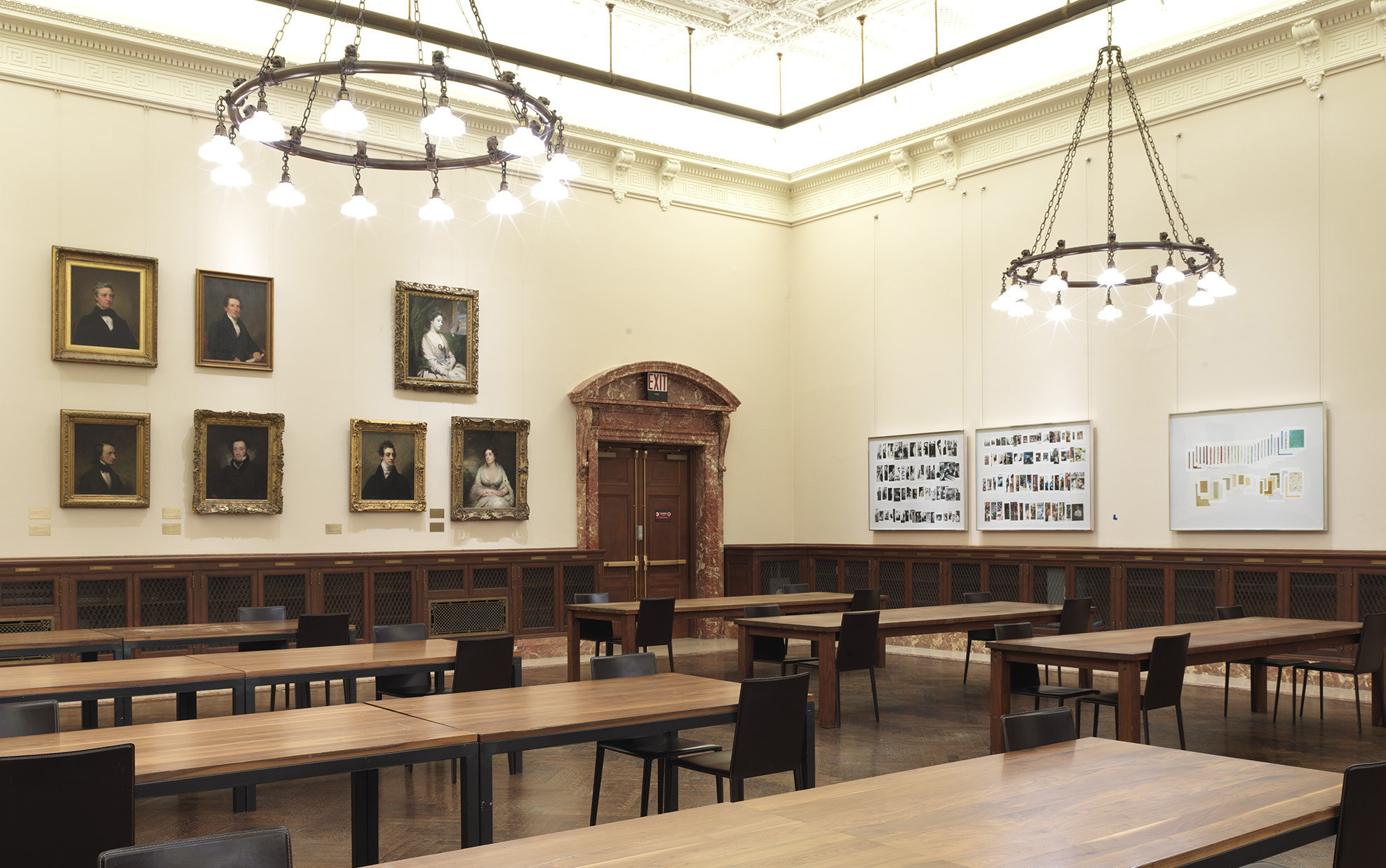 And empty library room with tables and chairs and paintings of men on one hand, Taryn's work hanging on the right
