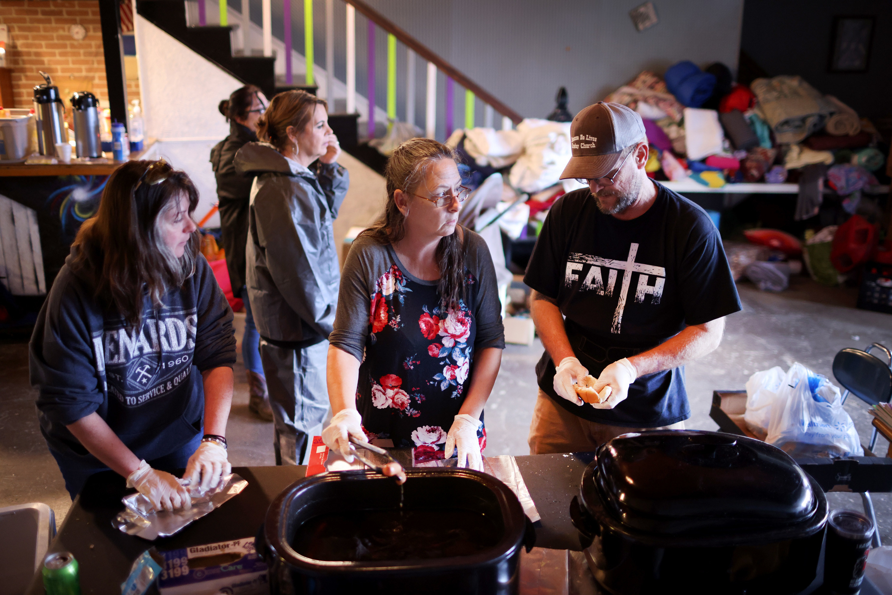 Three women and one man prepare food to distribute to the needy in kentucky, a pile of clothing is behind them 