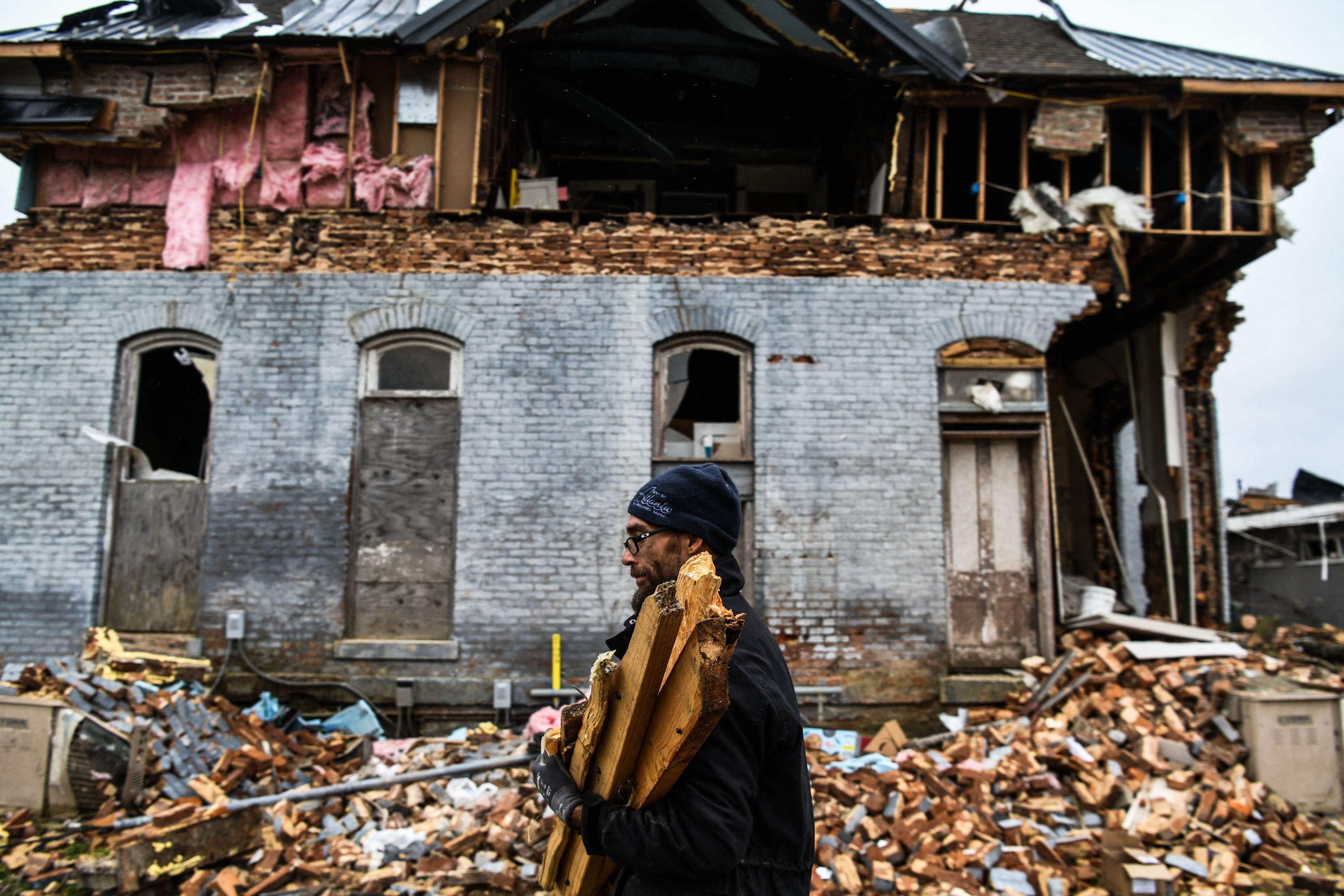 A man carries boards past a destroyed house and pile of bricks after the tornado