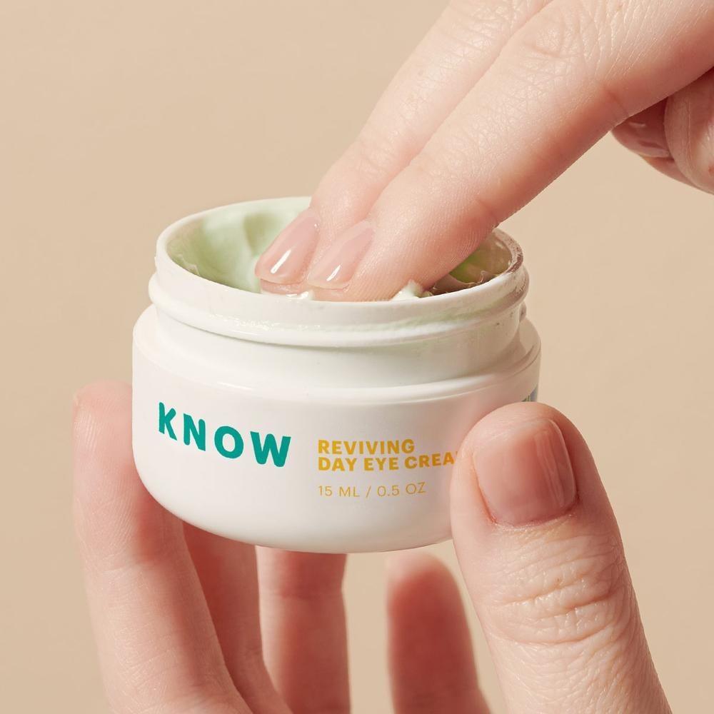 Model holding Know Beauty eye cream with fingers scooping product out of jar