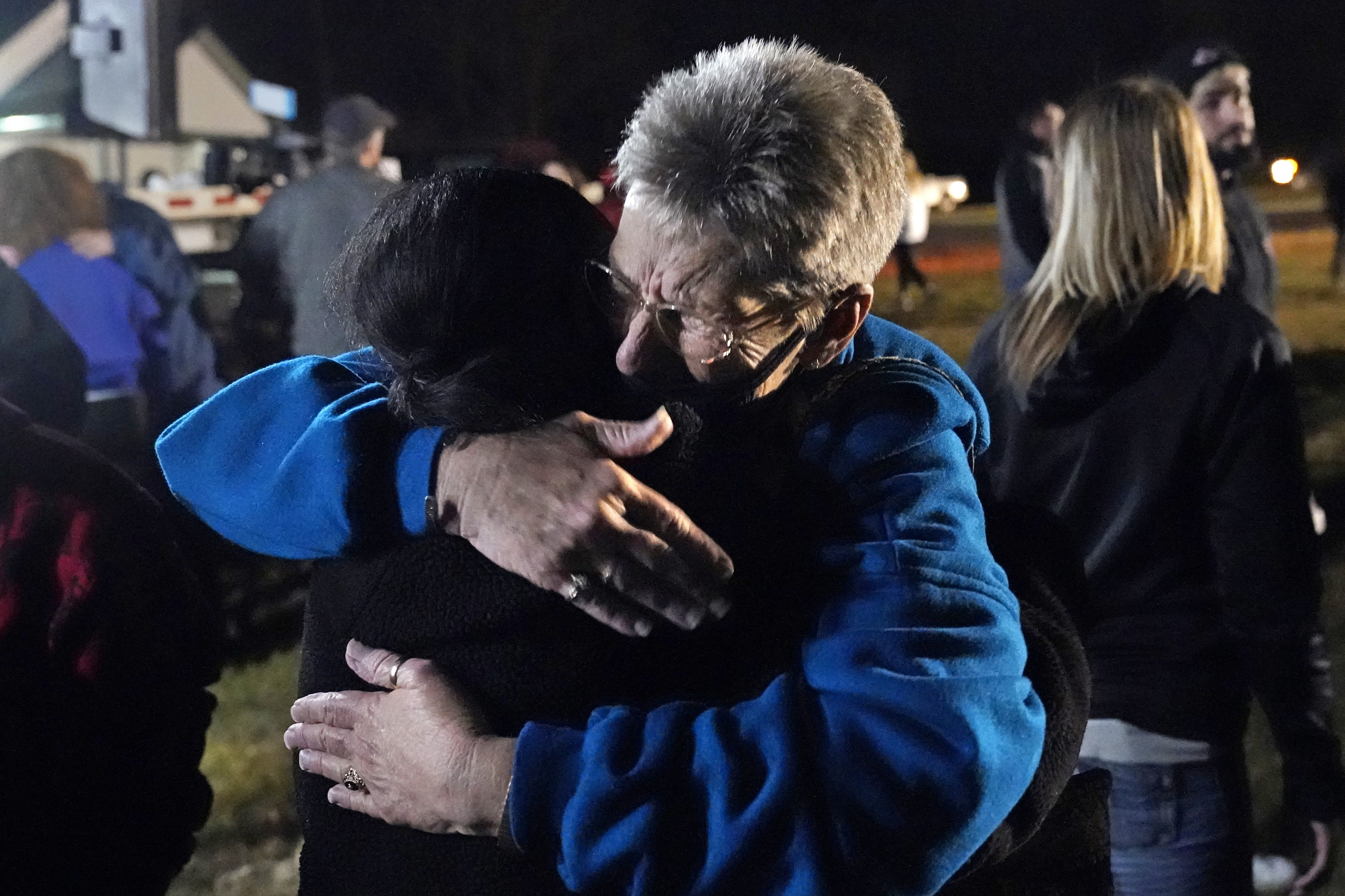 A woman hugs another woman at a vigil outside at night in kentucky 