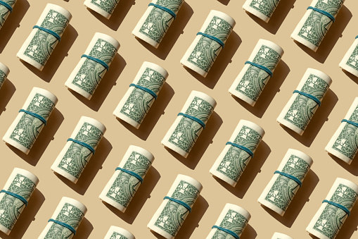 Rolled dollar bills in rubber bands on a beige background.