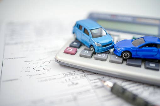 Toy cars sit on a calculator on top of insurance forms.