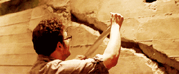 Seth Rogen putting a small piece of duct tape on a large crack in a wall