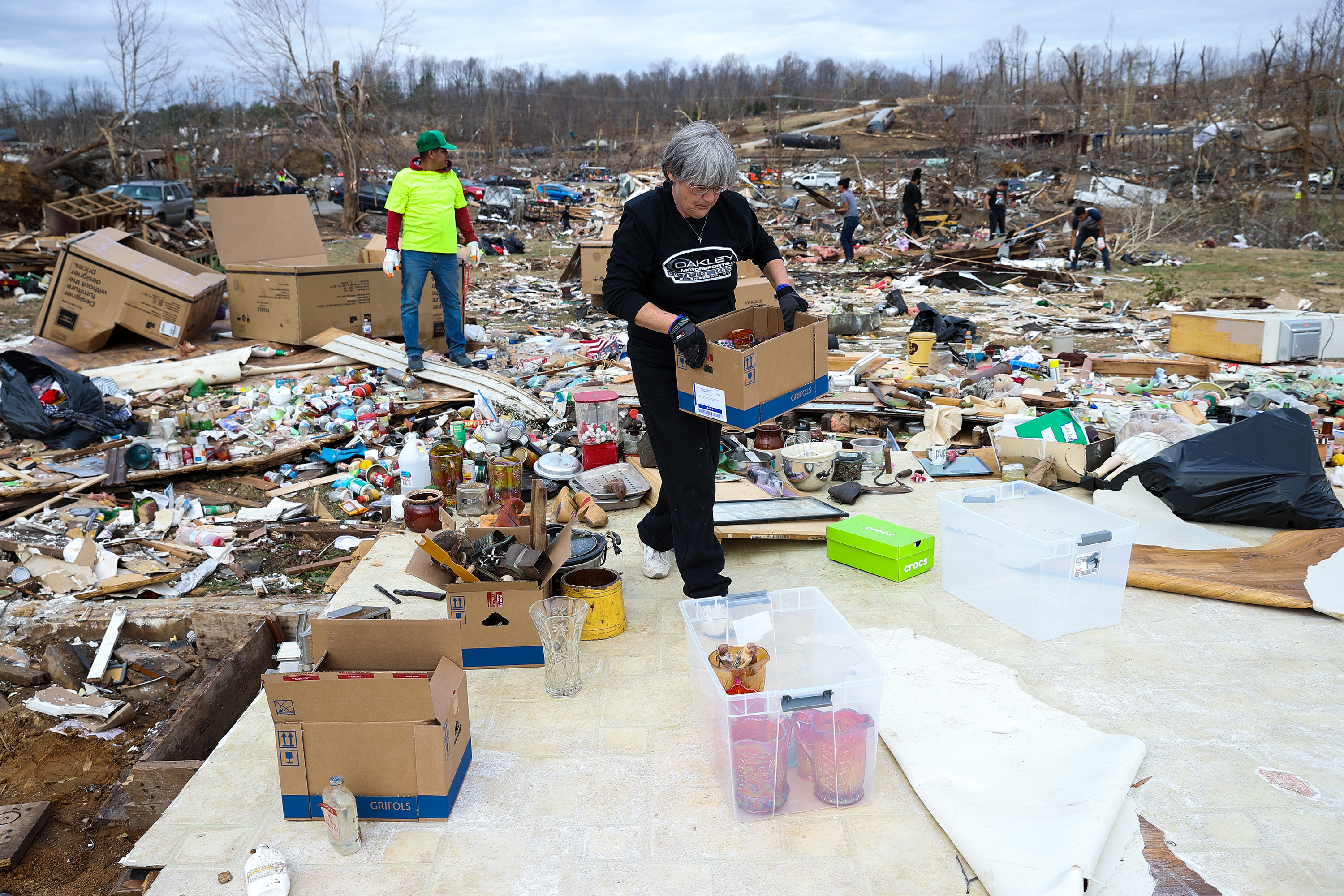 A woman passes a box of belongings over to a flat area over at her destroyed home 