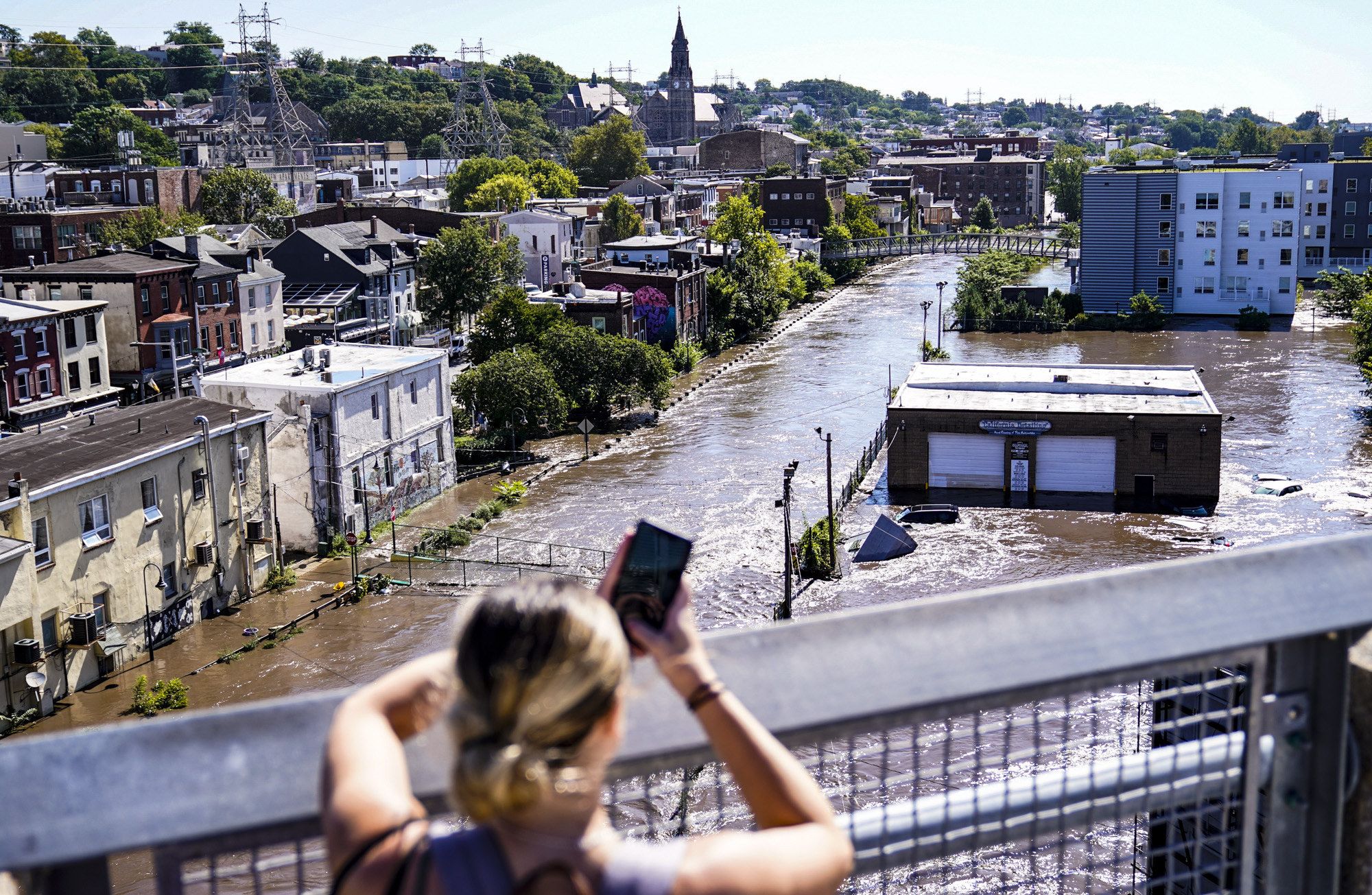 A woman takes a cellphone photo of a flooded street from an overpass bridge 