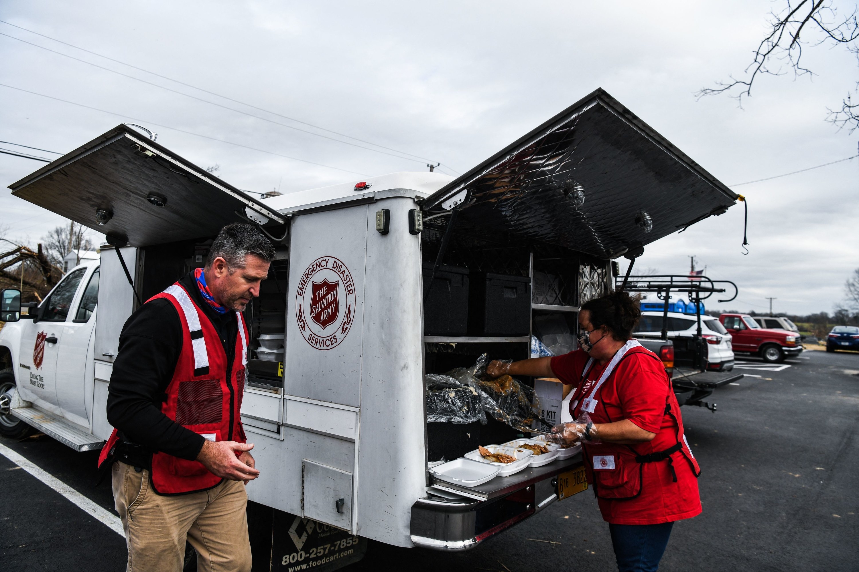 A man and woman in safety vests outside a salvation army emergency disaster truck distributing food