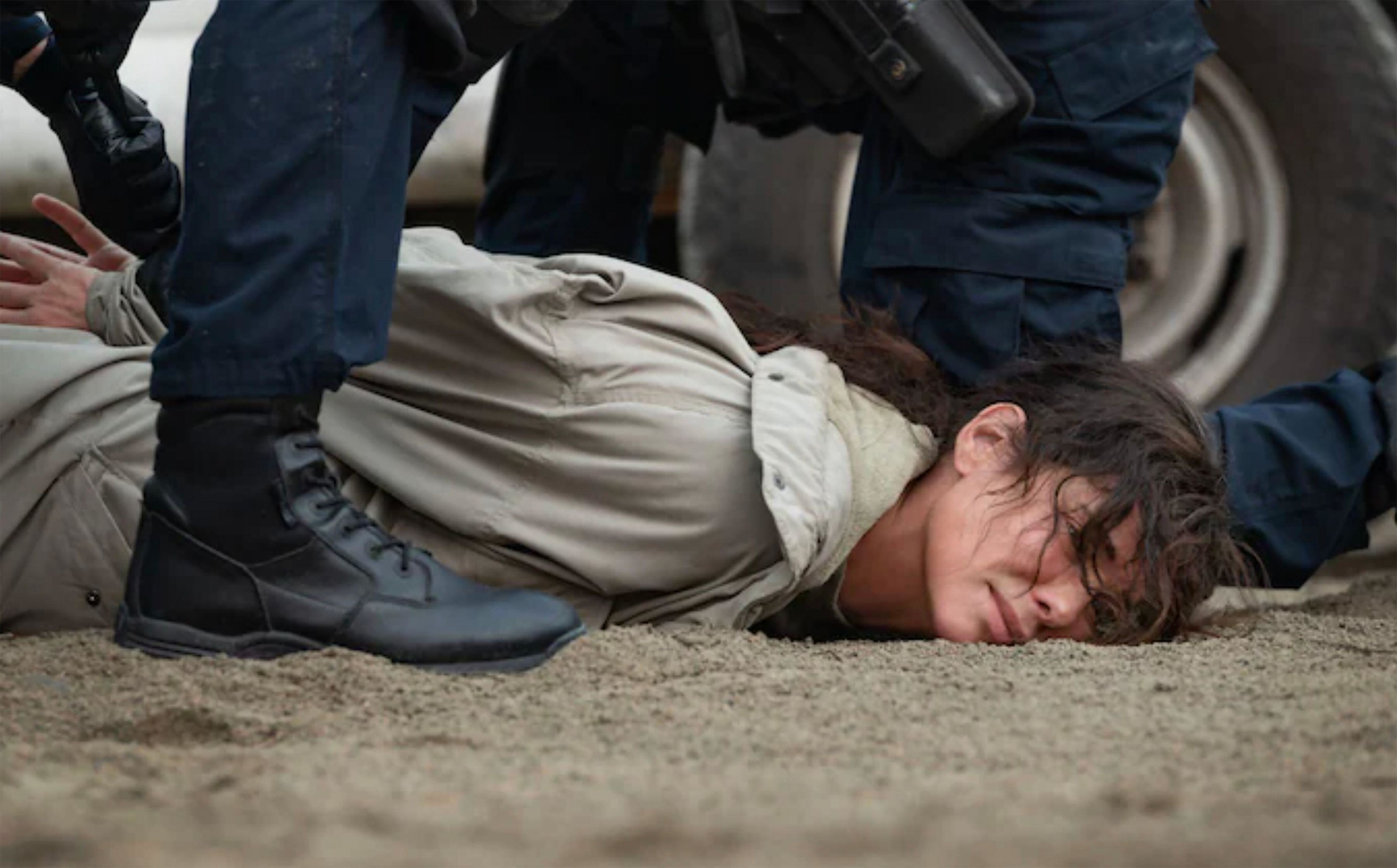 A woman is on her belly with her hands behind her back as police apprehend her.