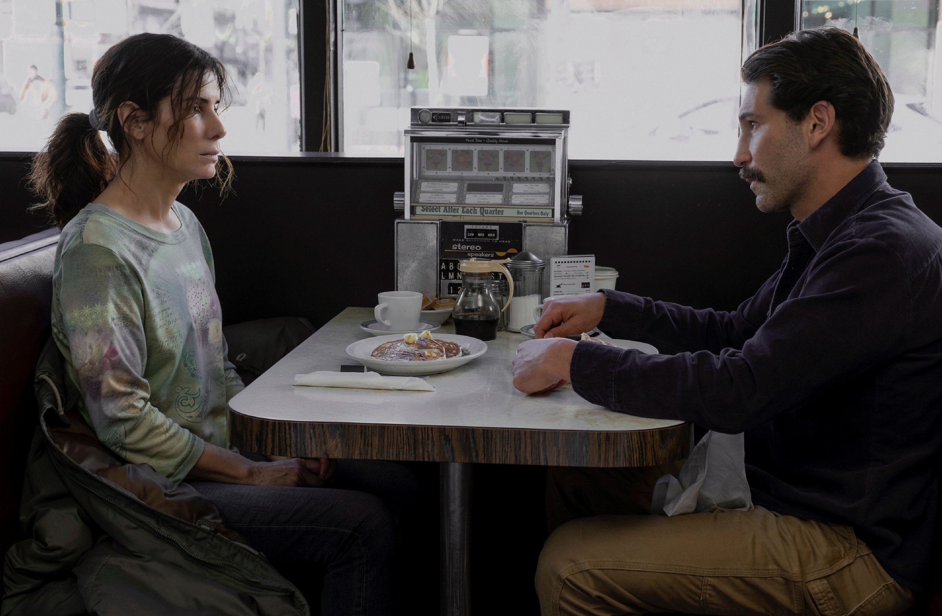 A woman sits a across a man at a diner with a plate of pancakes in between them