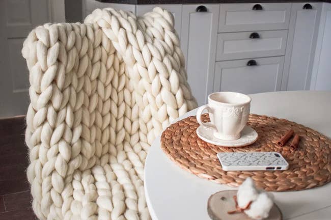 The chunky knit blanket in ivory laying on a chair