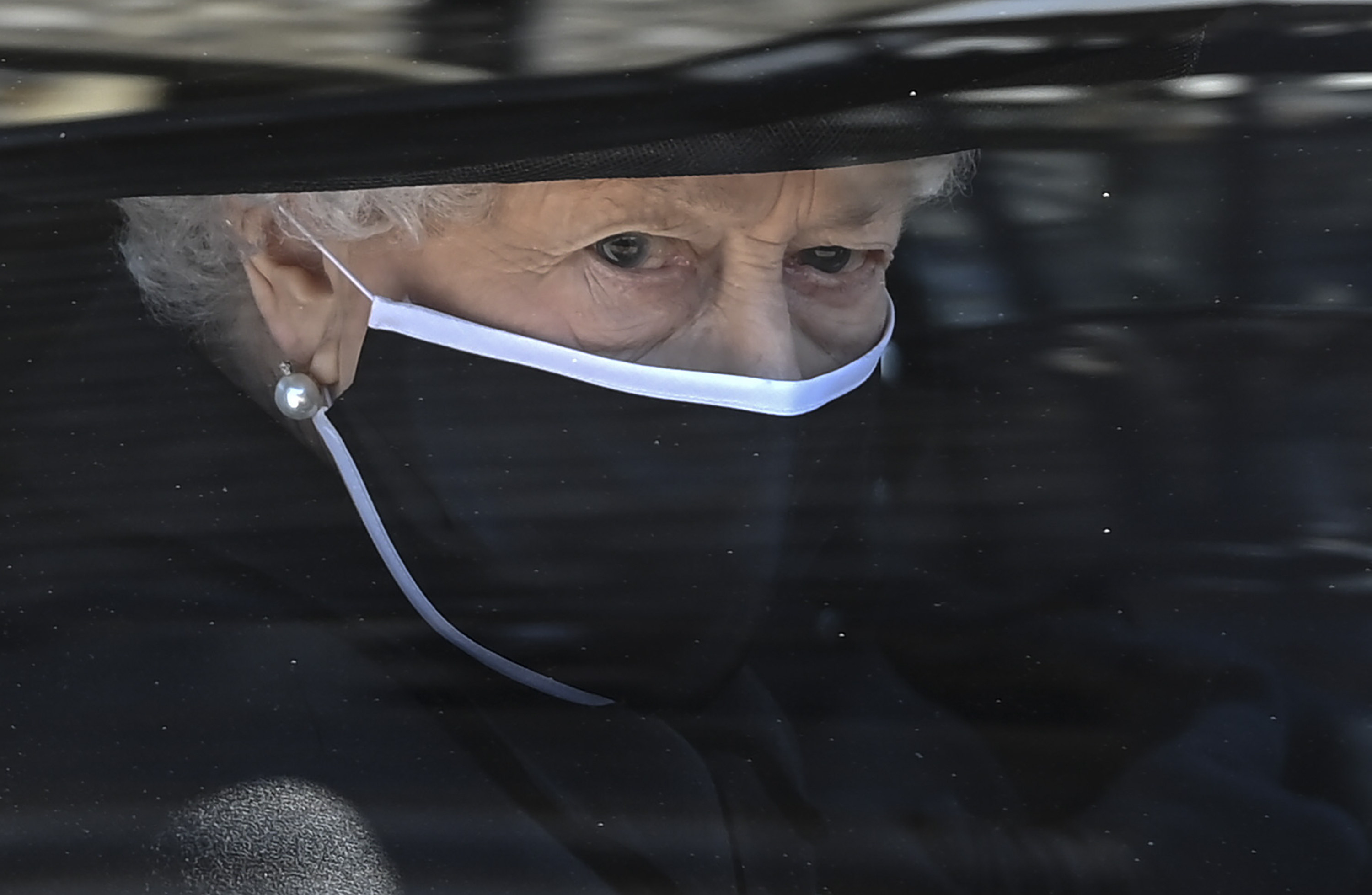The queen in black in a mask seen looking out from a car window
