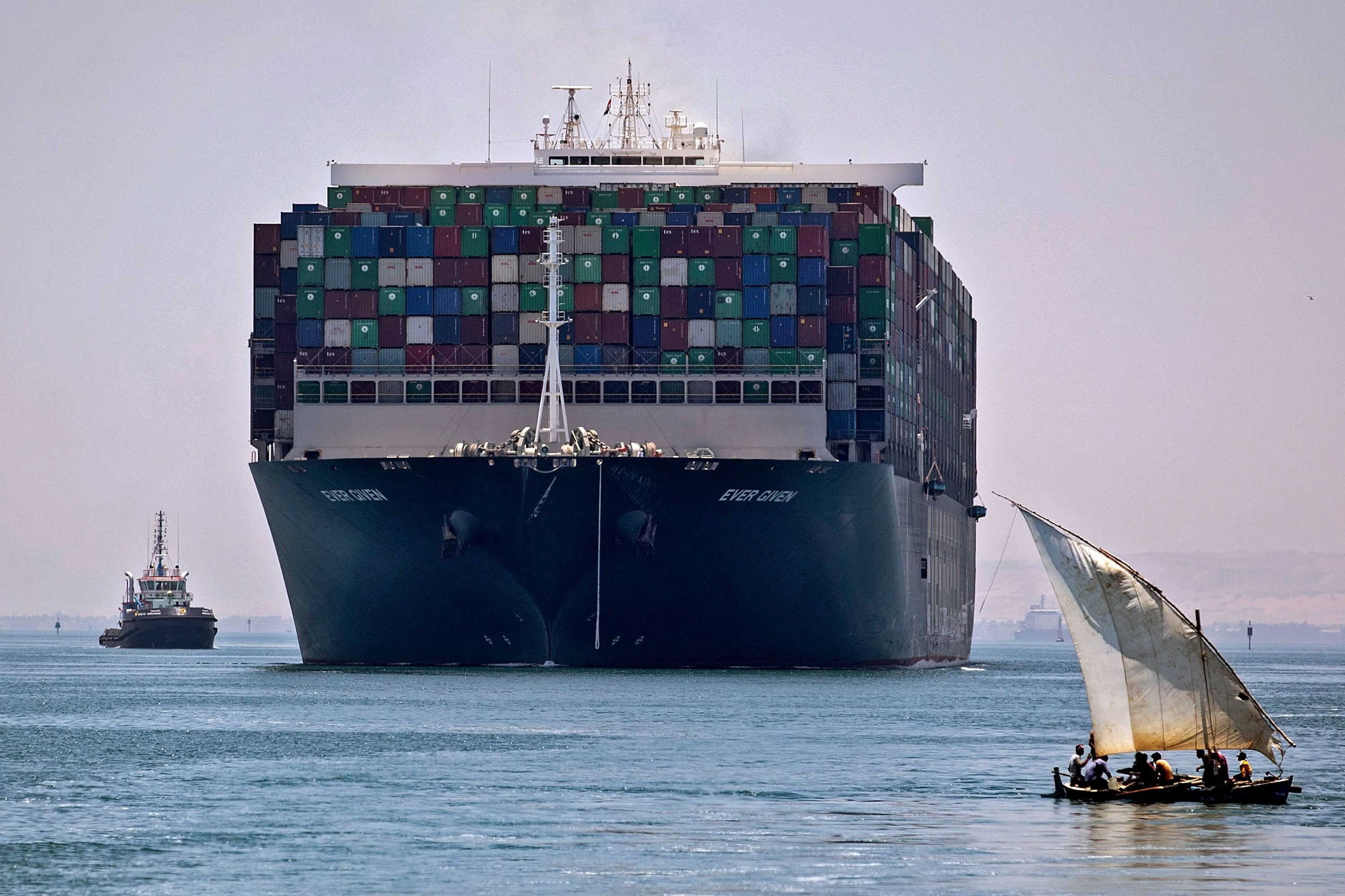 A giant container ship seen going through a canal with a smaller traditional dhouw in the foreground