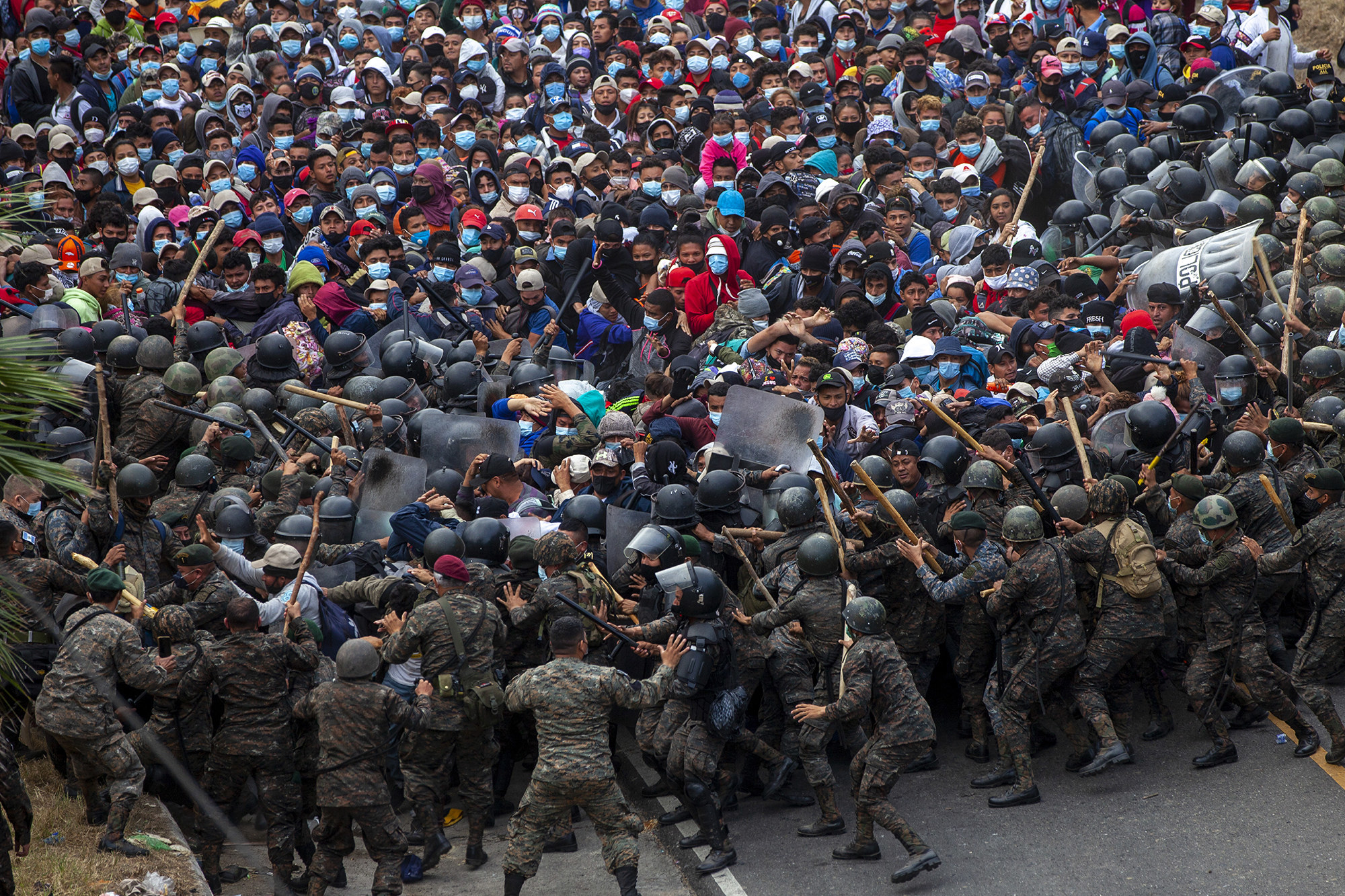 A huge crowd of people is held back by soldiers in riot gear wielding batons