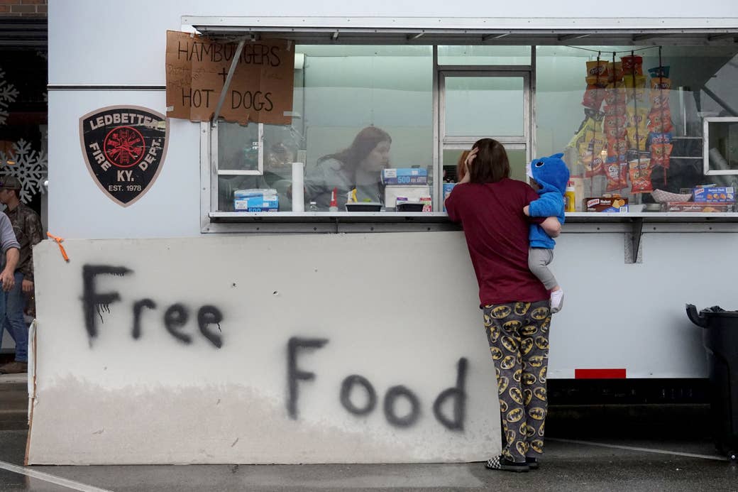 A woman holds a toddler next to a building that has free food spray painted outside of it