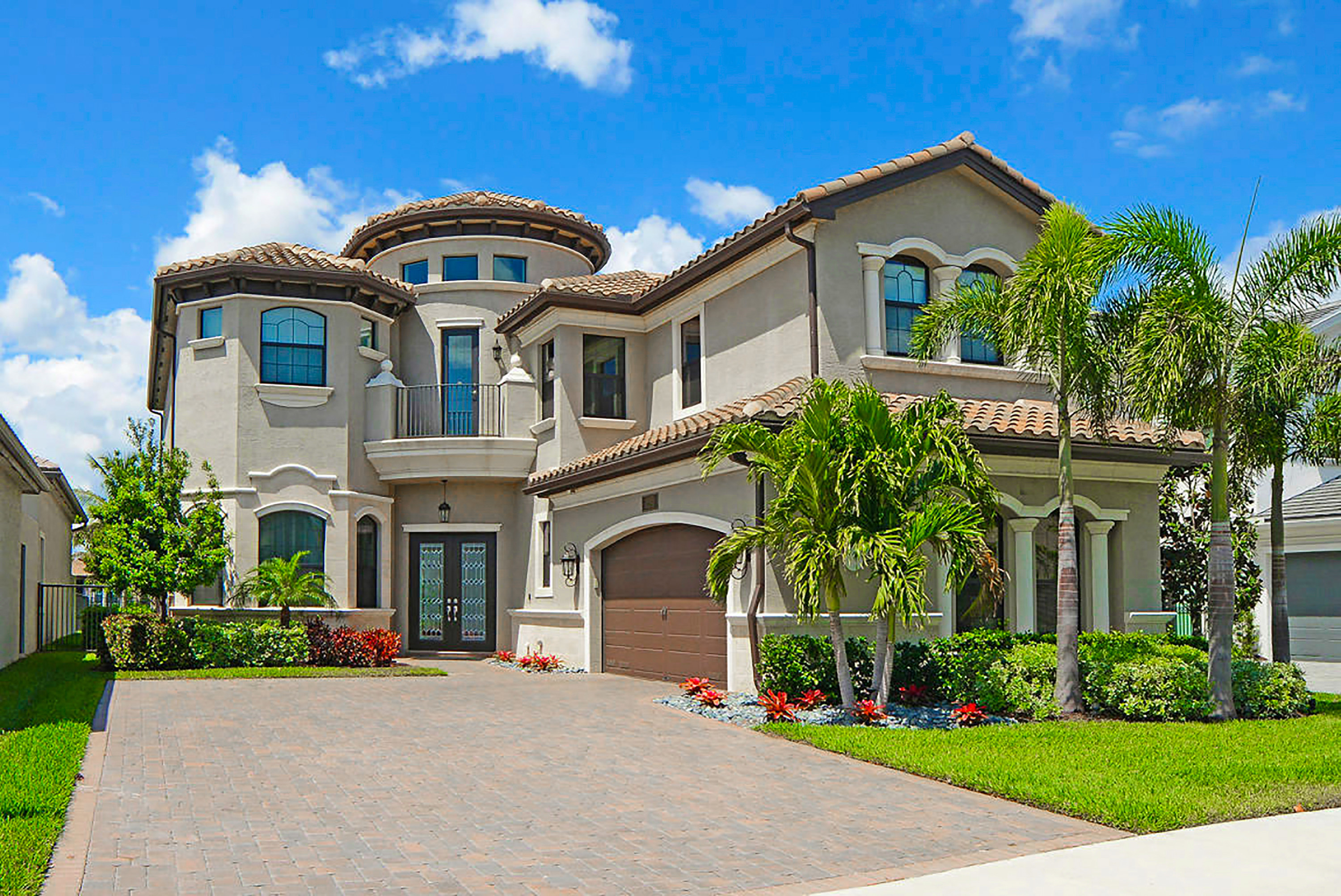 McMansion-style home with large driveway and palm trees in a housing development