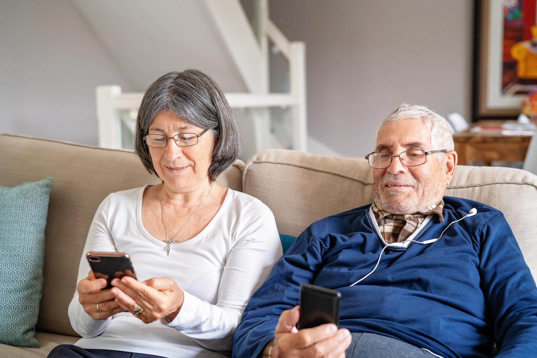 Older woman and man sitting on a couch smiling and looking at their cellphones