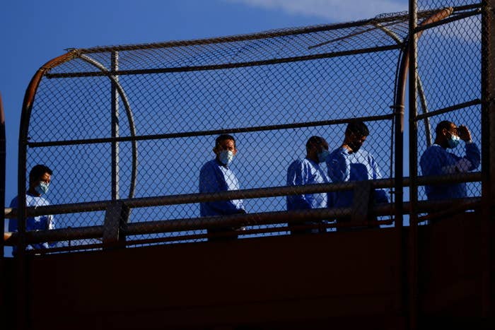 People wearing masks stand inside a wire fence enclosure