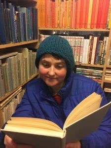 A candid pic of me sitting in a bookstore in Iceland, reading a book. I'm wearing a blue knit hat and a blue puffer jacket.