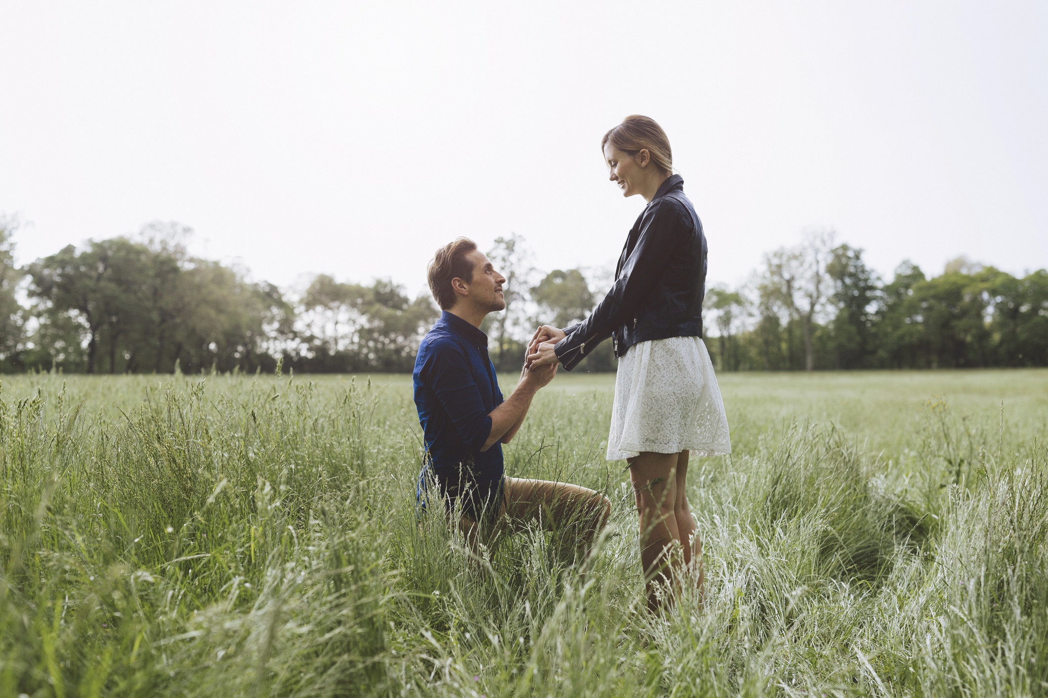 Man on one knee in front of a woman in the middle of a bunch of grass