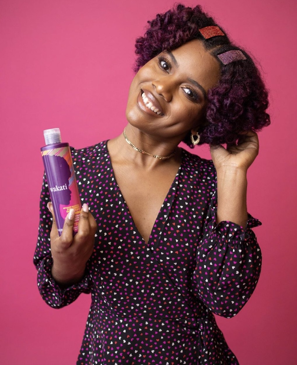 A person wearing a multicolored heart dress holding a bottle of detangling conditioner
