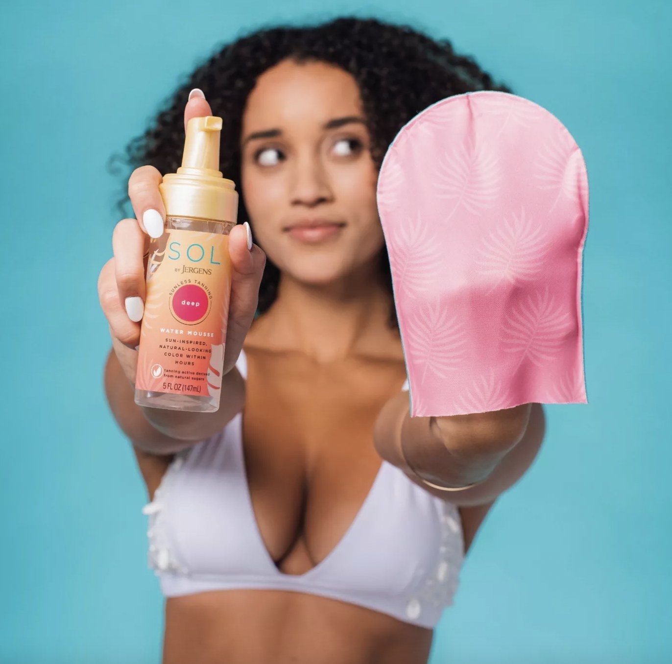 A person holding a tanning product and a mitt
