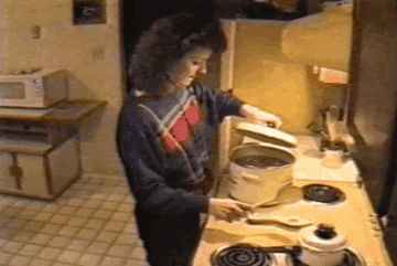 a woman takes the lid off of a pot on the stove, only for a hand to reach at her, causing her to jump back and drop the lid