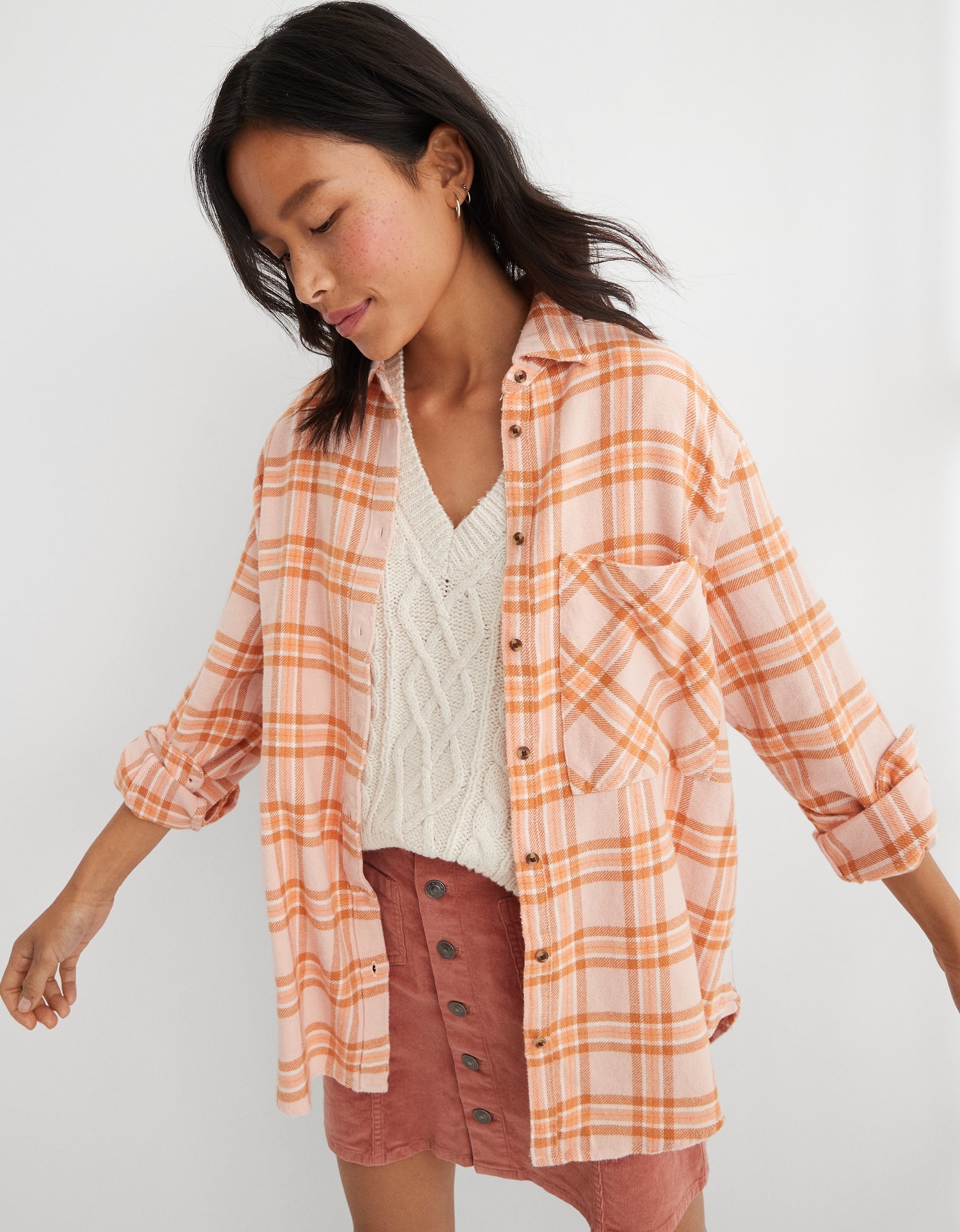 model in orange and pink flannel button-up over a sweater vest