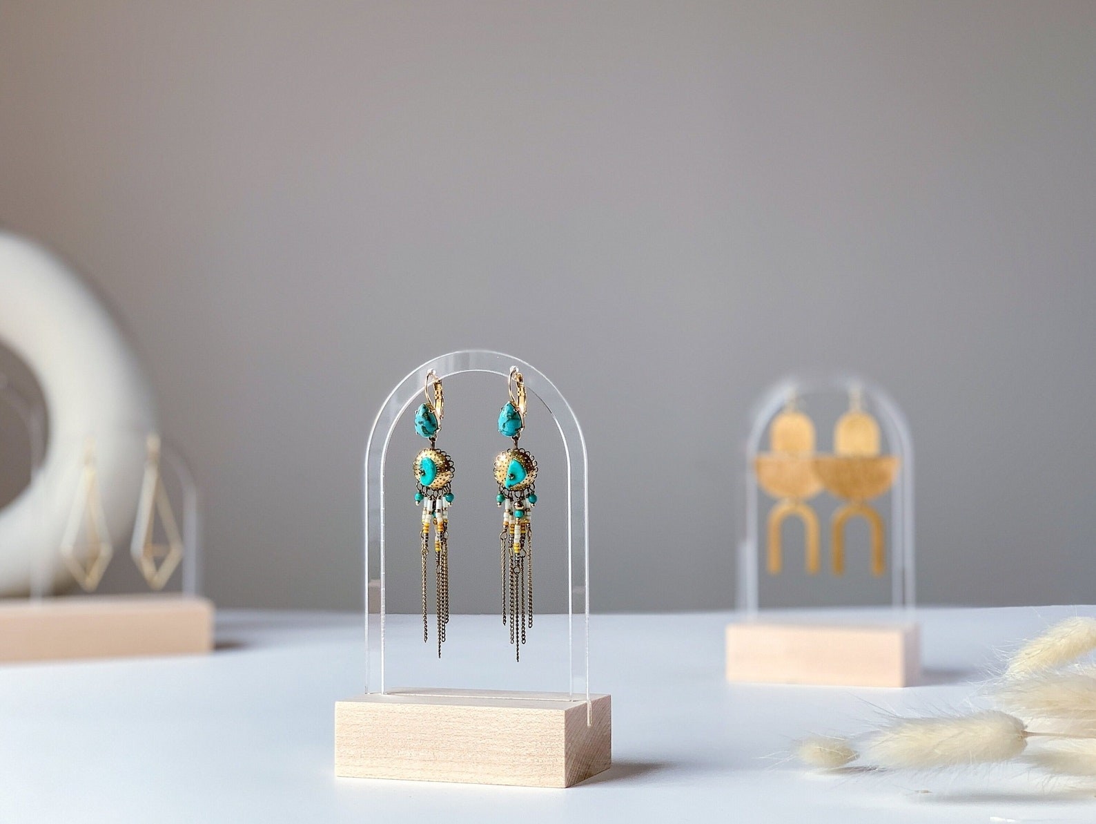 A pair of earring hanging from a small acryrlic display with a wooden base