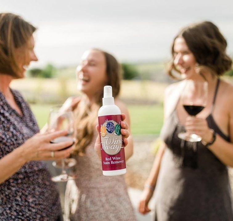 a person holding up a bottle of the red wine stain remover while laughing with their friends