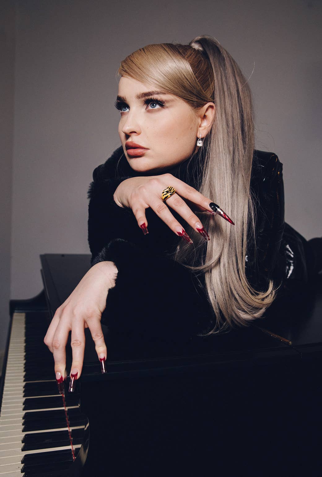 Kim Petras on top of a piano playing it casually with very long nails
