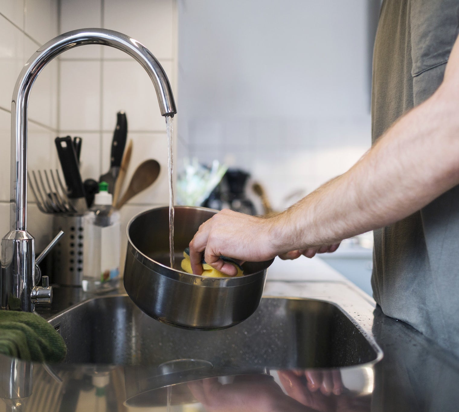 man washing sauce pan with sponge at sink.