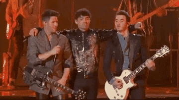 Joe Jonas putting arms around Nick Jonas on left and Kevin Jonas on right