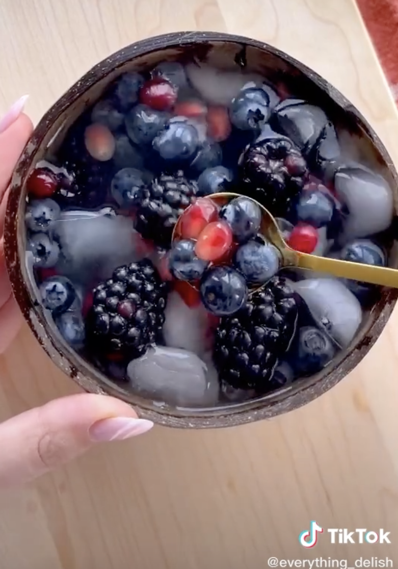 A bowl of coconut water, ice, blackberries, blueberries, and pomegranate seeds