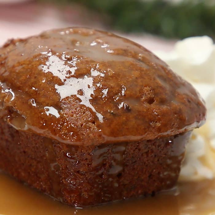 A close up shot of a mini Sticky Toffee Pudding with a glaze on top. Sitting next to whip cream.