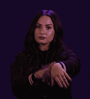 Demi Lovato gesturing to an imaginary watch on her wrist