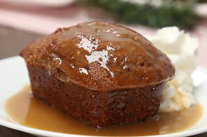 A close up shot of a mini Sticky Toffee Pudding with a glaze on top. Sitting next to whip cream.