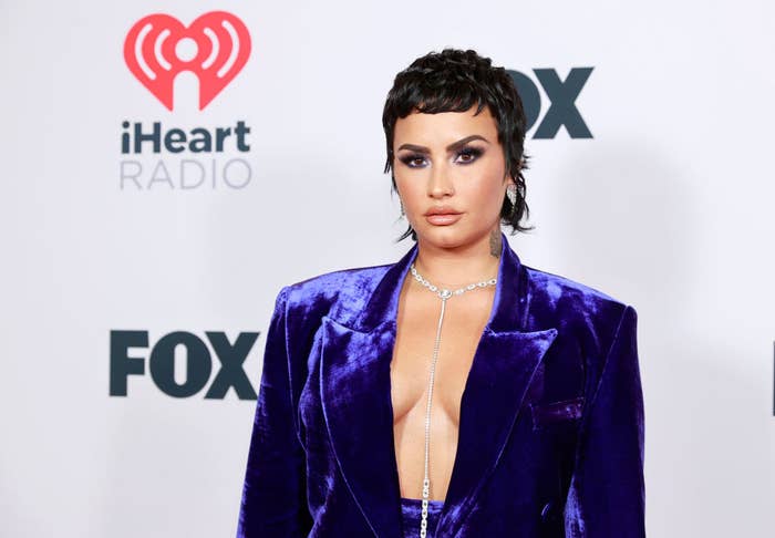 Demi poses on the red carpet of an event in a velvet suit and a long chain necklace