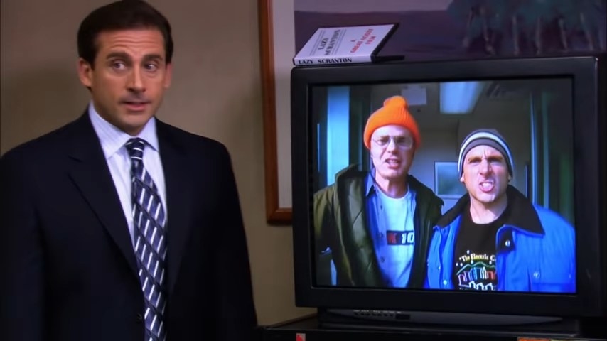 Michael standing next to a TV playing a video of him and Dwight in &quot;The Office&quot;