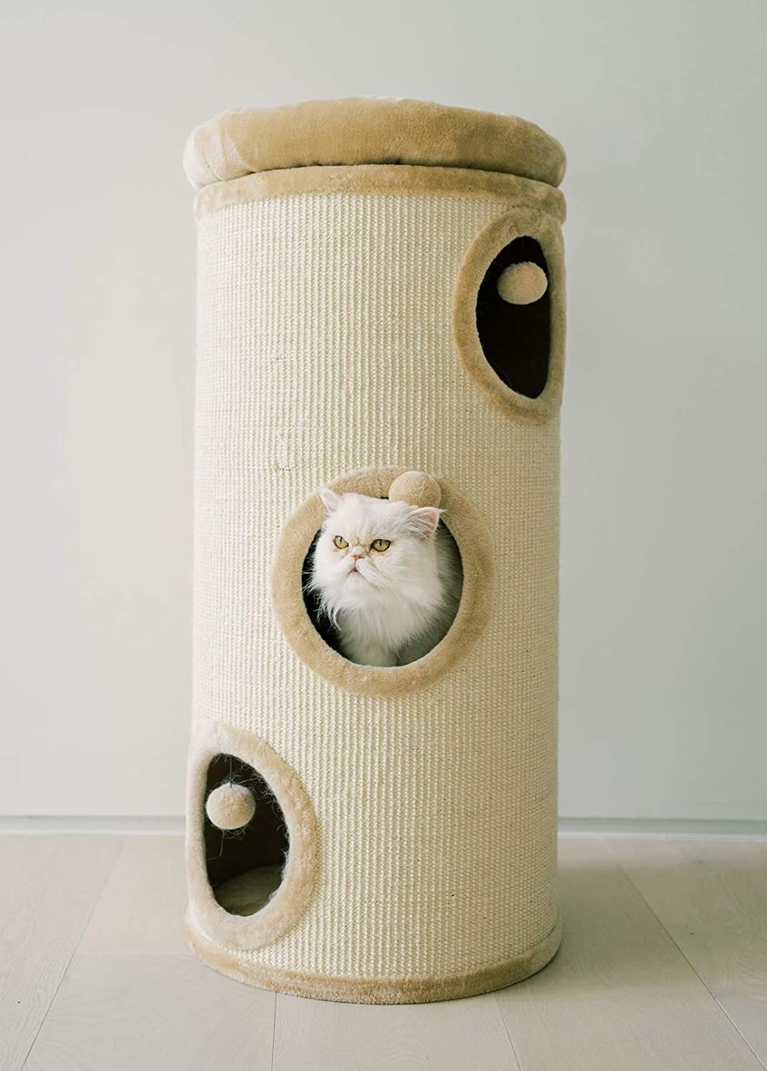 tan cylindrical cat tower with sisal sides, a bed on top, and three circles on each level to allow the cat to jump inside