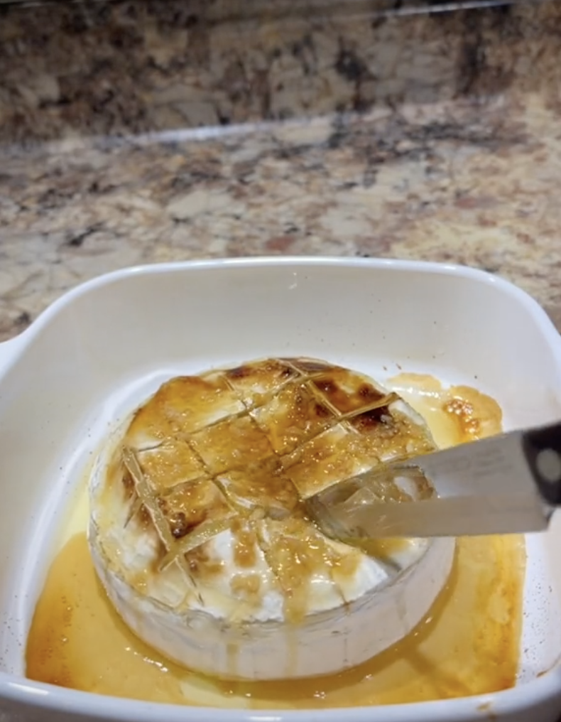 Someone cutting into a baked brie