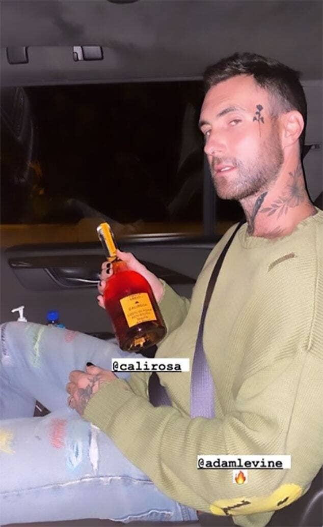 Adam holds a bottle of alcohol while displaying a rose tattoo on the side of his face