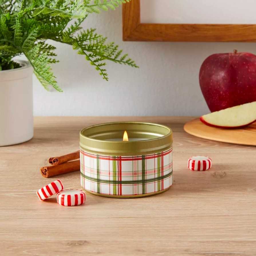 Plaid tin candle next to peppermint candies and cinnamon sticks
