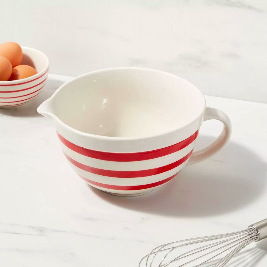 Striped red and white batter bowl next to a bowl of eggs and a whisk