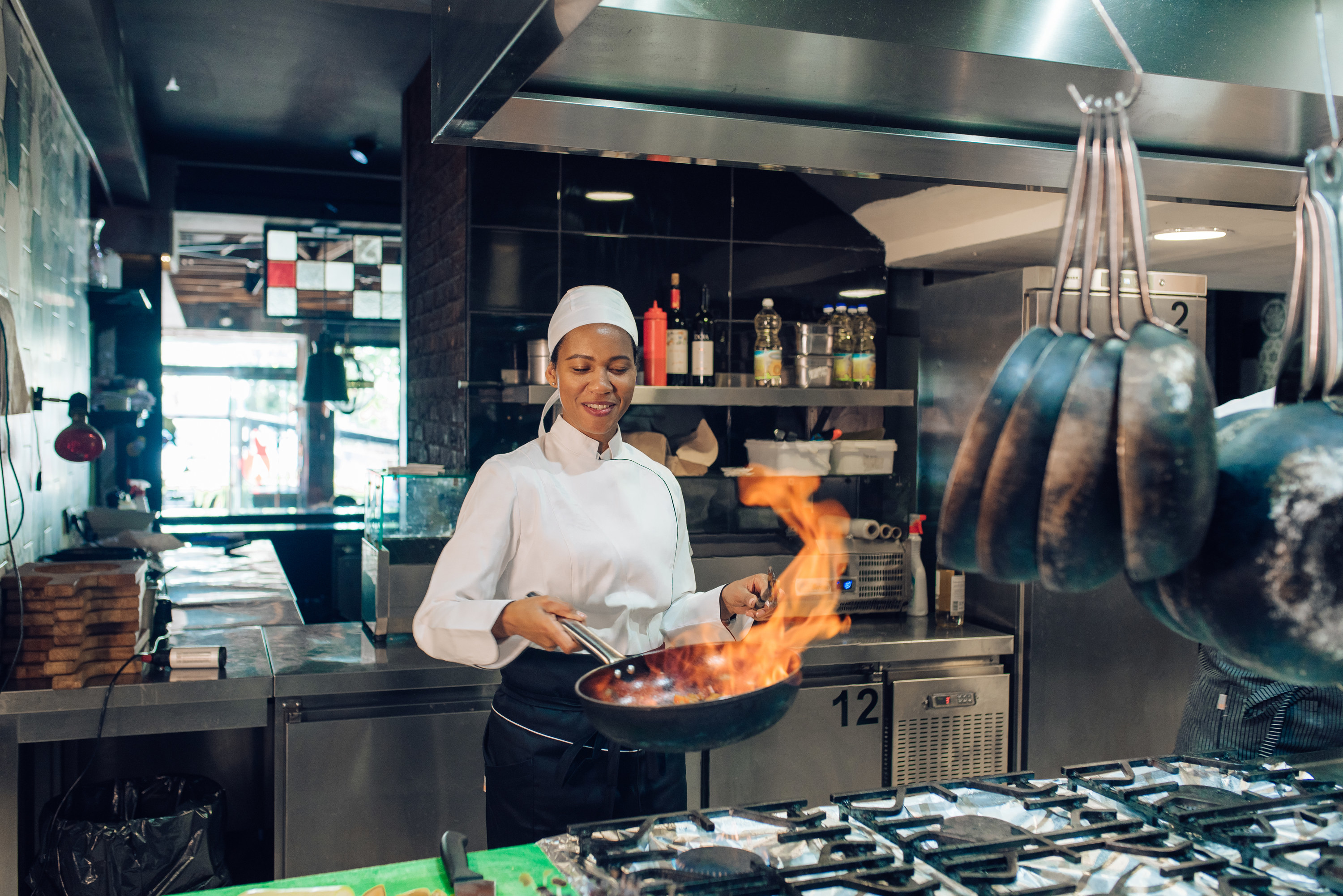 Female chef flambéing food in a restaurant kitchen
