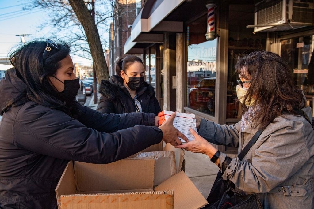 A person handing someone several boxes of at-home tests from a box