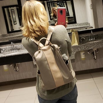 reviewer wearing the khaki anti-theft backpack on their back