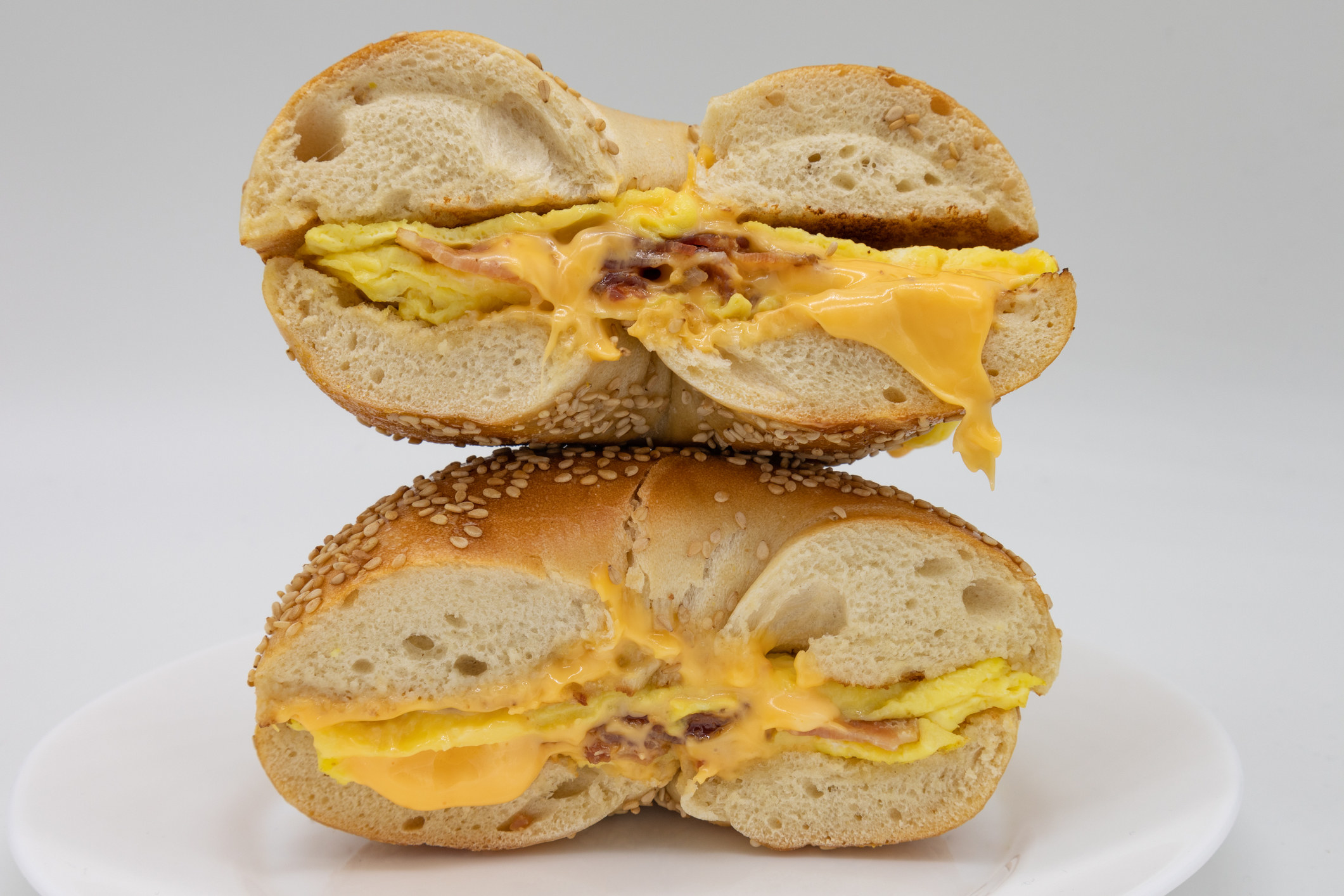 Sesame Seed Bagel Cut in Half with Bacon Eggs and Cheese on a White Plate.